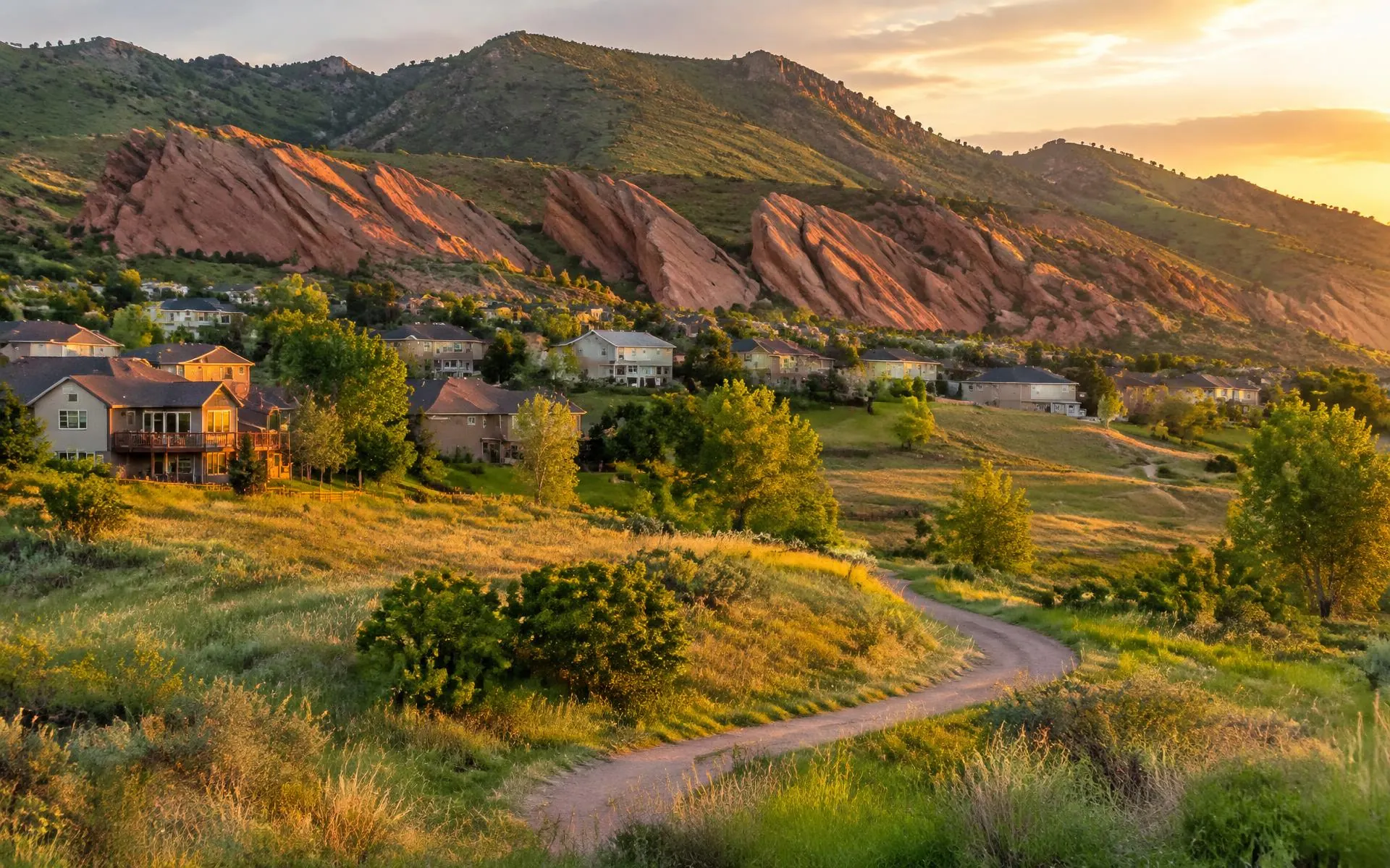 Ken Caryl Colorado homes below red rock formations and green foothills with a trail winding through open space at golden hour