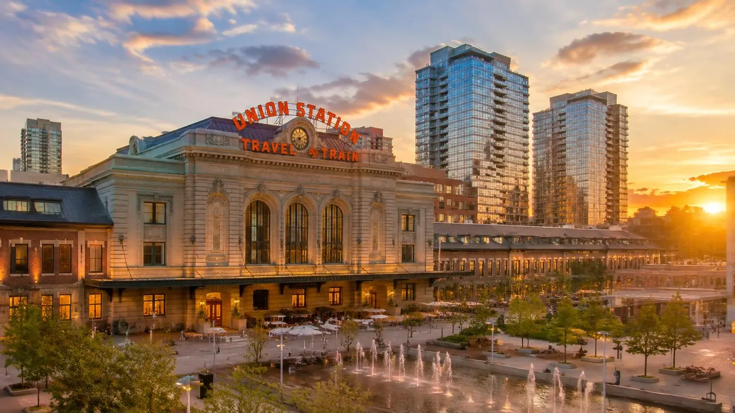 Historic Denver Union Station facade and plaza fountains at sunset with modern residential towers behind